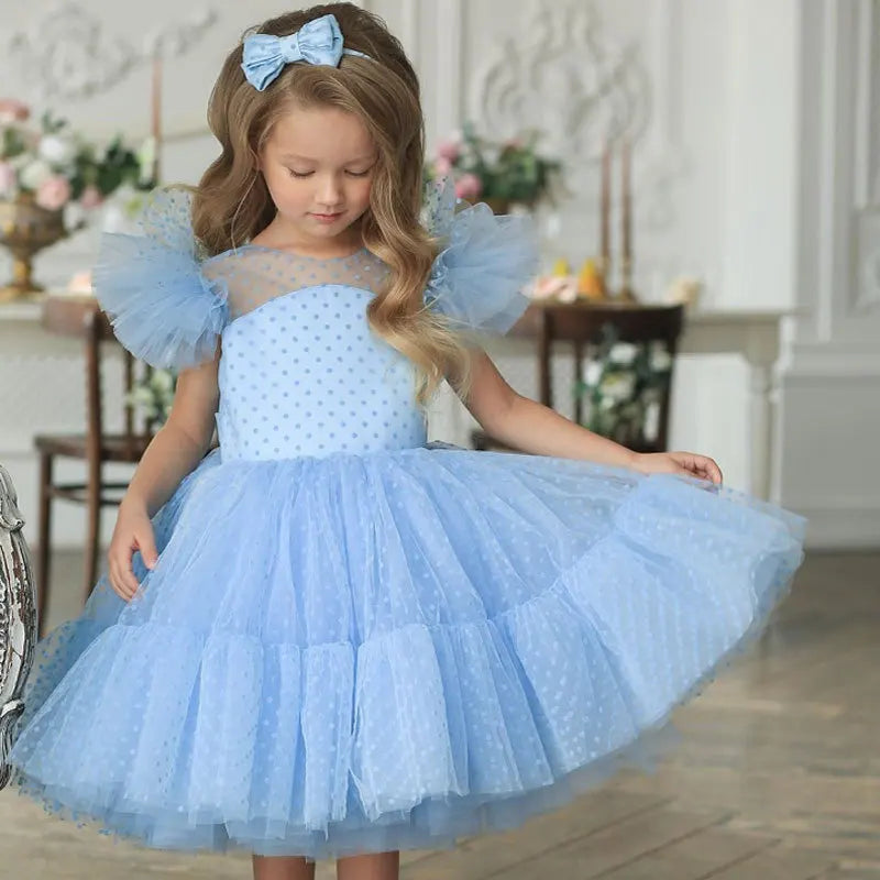 Cute girl wearing the 'Ashlyn' Dotted Swiss Dress in baby blue, featuring ruffled butterfly sleeves and a full skirt, perfect for special occasions.